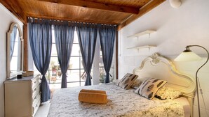 Een slaapkamer met een bed, gordijnen, een dressoir, een lamp en uitzicht.