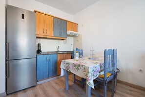 A compact kitchen with a stainless steel refrigerator, wooden cabinets, a tiled backsplash, and a dining table with chairs. - Vacation Home "Tanai" close to the Beach with Private Terrace (El Cotillo)