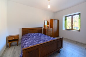 A bedroom with a wooden bed, a nightstand, a wardrobe, and a window with curtains.