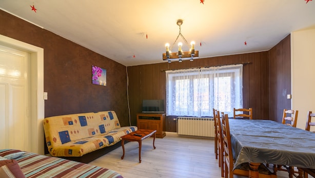 Ett vardagsrum med en soffa, ett matbord, stolar, en tv och ett fönster med gardiner.