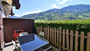 Un patio con una mesa y sillas, una valla de madera y vistas a una montaña boscosa.