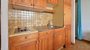 Una cocina compacta con armarios de madera, un lavamanos de acero inoxidable y un salpicadero de azulejos.