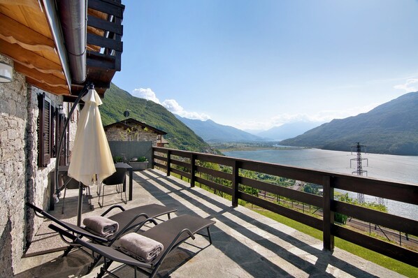 Un balcón con sillones, una mesa y vistas a un lago y montañas.