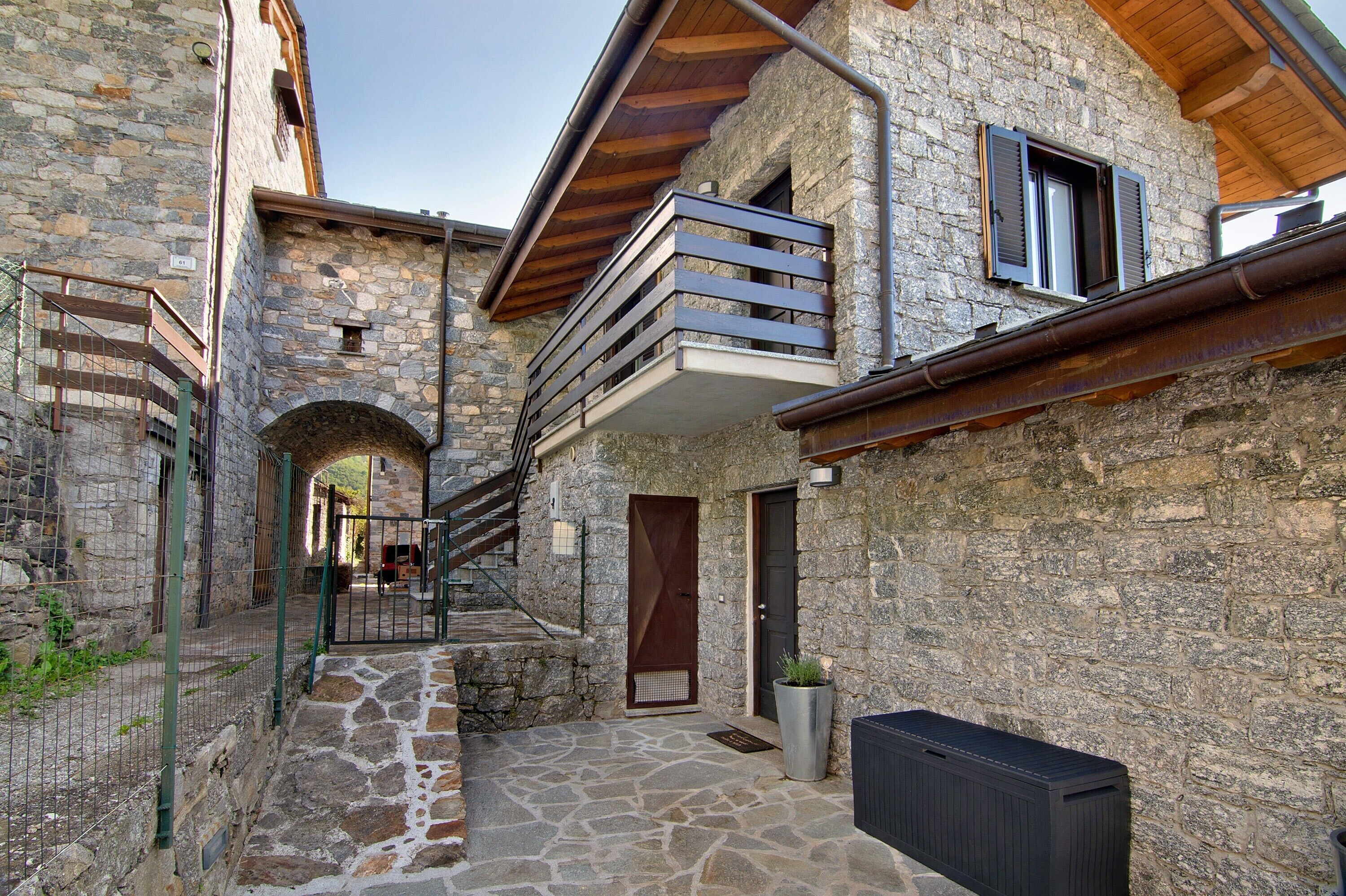 A stone building with a balcony, a door, and a small garden area.