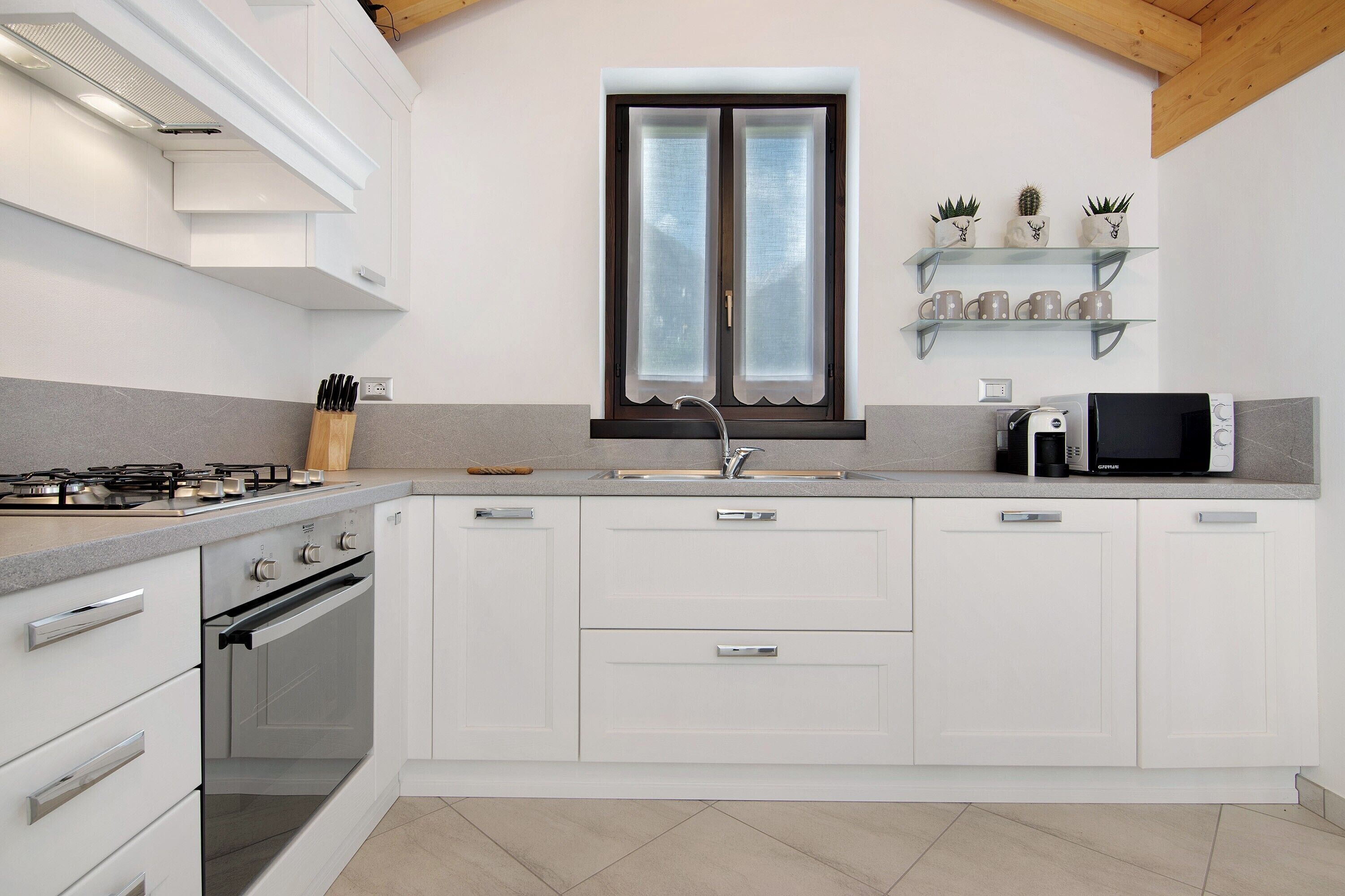Une cuisine moderne avec des armoires blanches, un four encastré, une cuisinière à gaz, un four à micro-ondes et une fenêtre à vitre dépolie.
