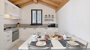 Una cocina moderna con armarios blancos, una mesa de comedor preparada para el desayuno y techo de madera.
