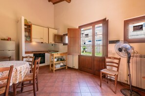 Una cocina compacta con mesa y sillas, un armario de madera, una ventana y un ventilador de pie.