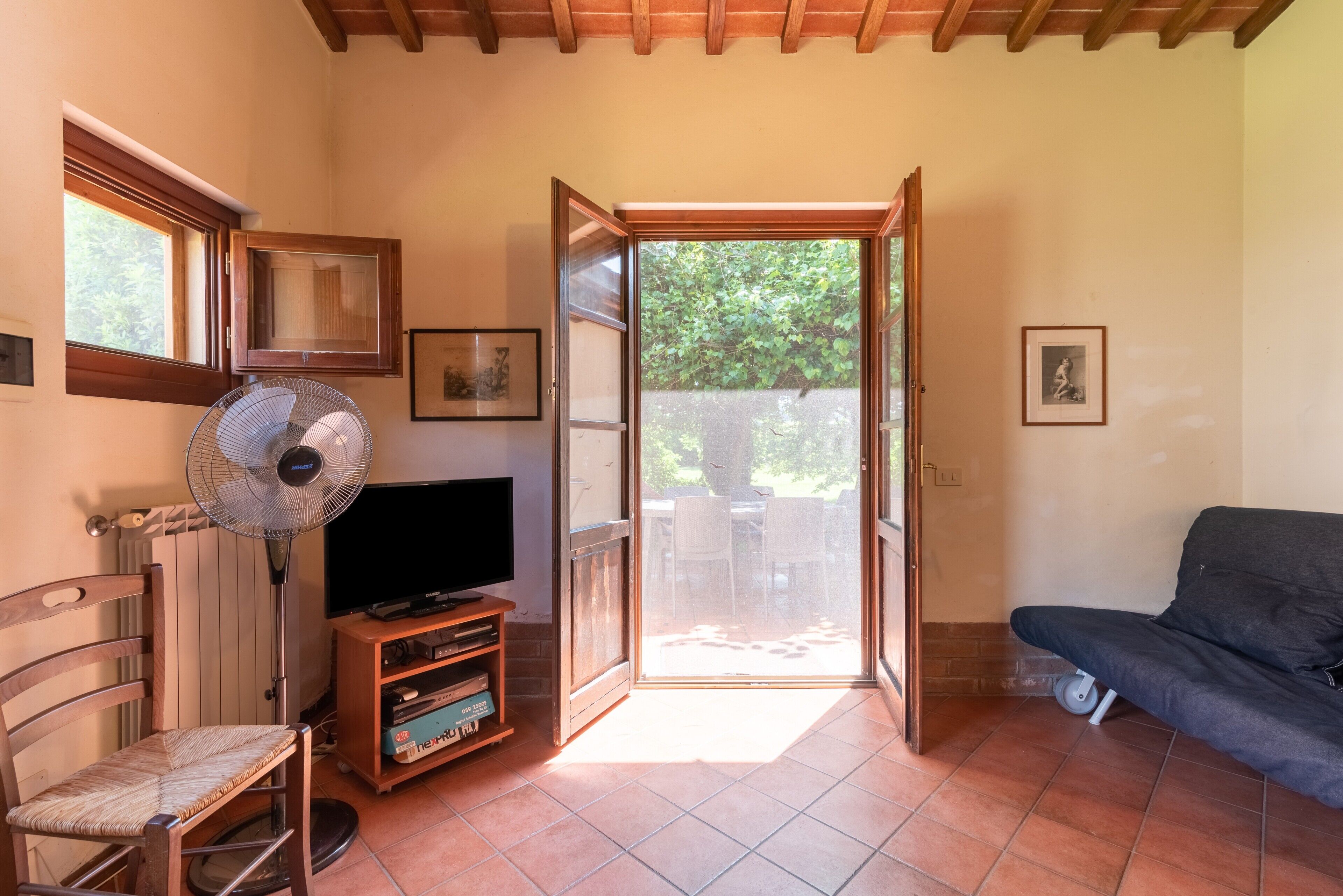 Une pièce équipée d’une télévision, d’un ventilateur, d’un canapé, d’une chaise et d’une porte-fenêtre coulissante donnant sur un espace extérieur.