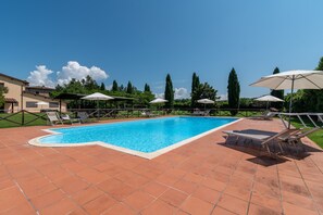 A swimming pool with tiled flooring, surrounded by lounge chairs and umbrellas, with trees and a building in the background. - Farmhouse "Officina" with Shared Pool, Private Terrace & Wi-Fi (Laterina)