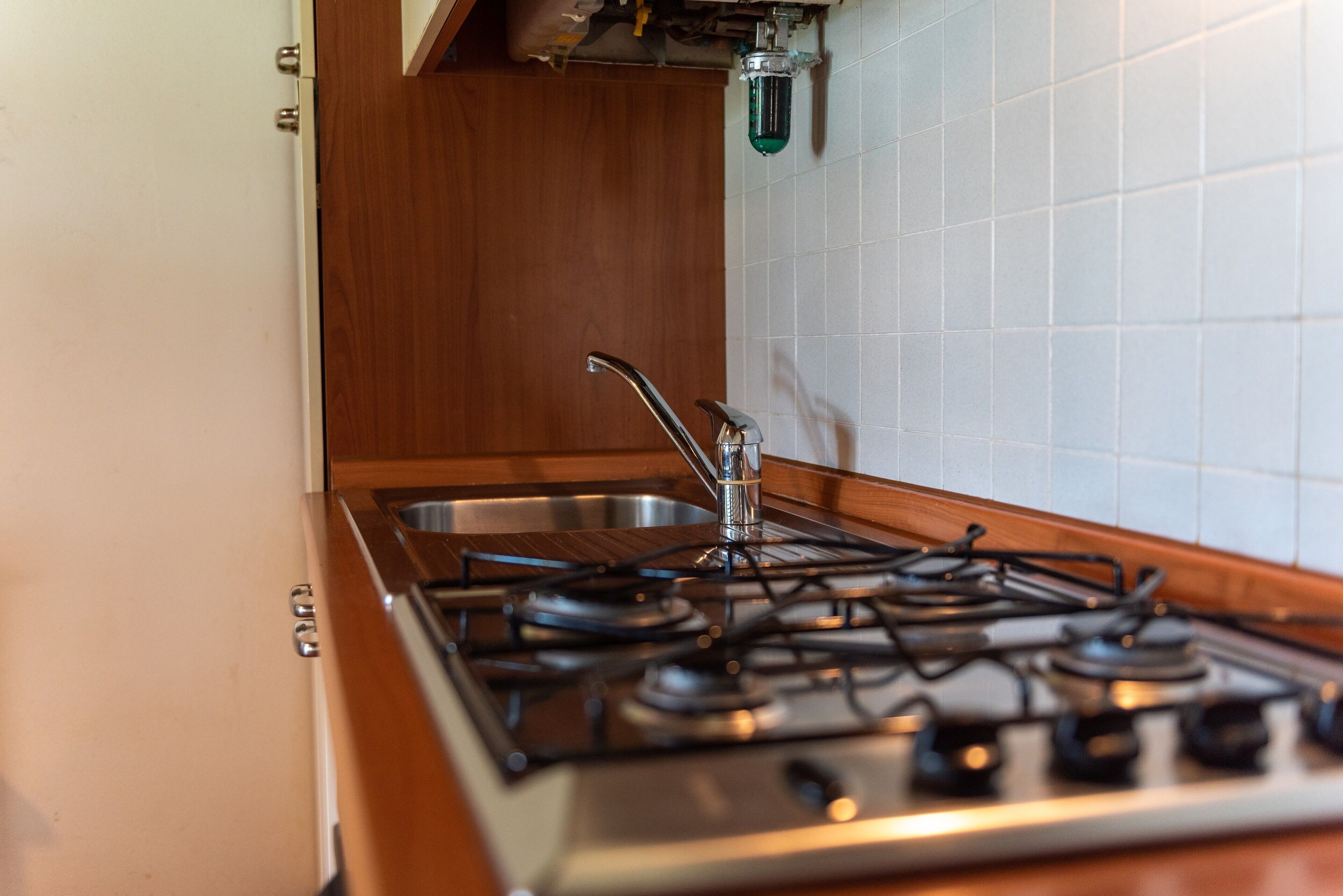 A kitchen with a gas stove, stainless steel sink, and wooden cabinetry.