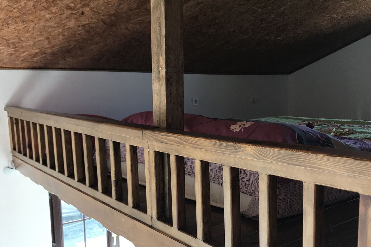 A loft-style room with a wooden bunk bed, a window, and a radiator.