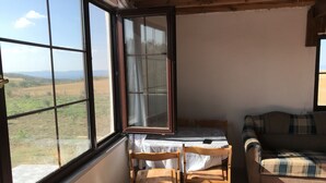 Ein Zimmer mit großem Fenster, einem Bett, einem Holzstuhl und einem karierten Sofa.