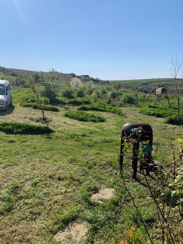 A rural landscape with a white vehicle parked on a dirt path, surrounded by greenery and hills.