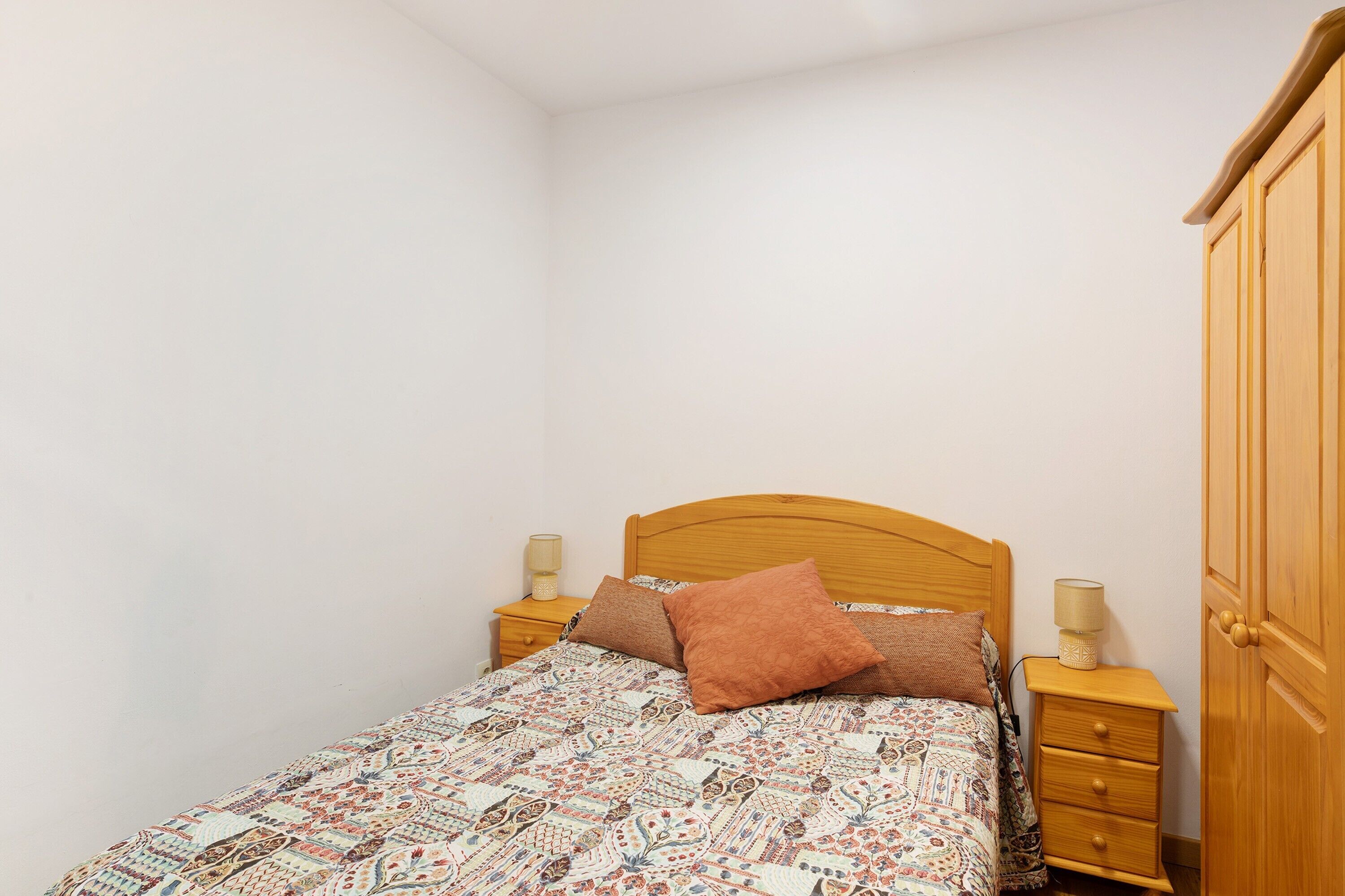 A bedroom with a wooden bed, two bedside tables, a nightstand, and a wardrobe.