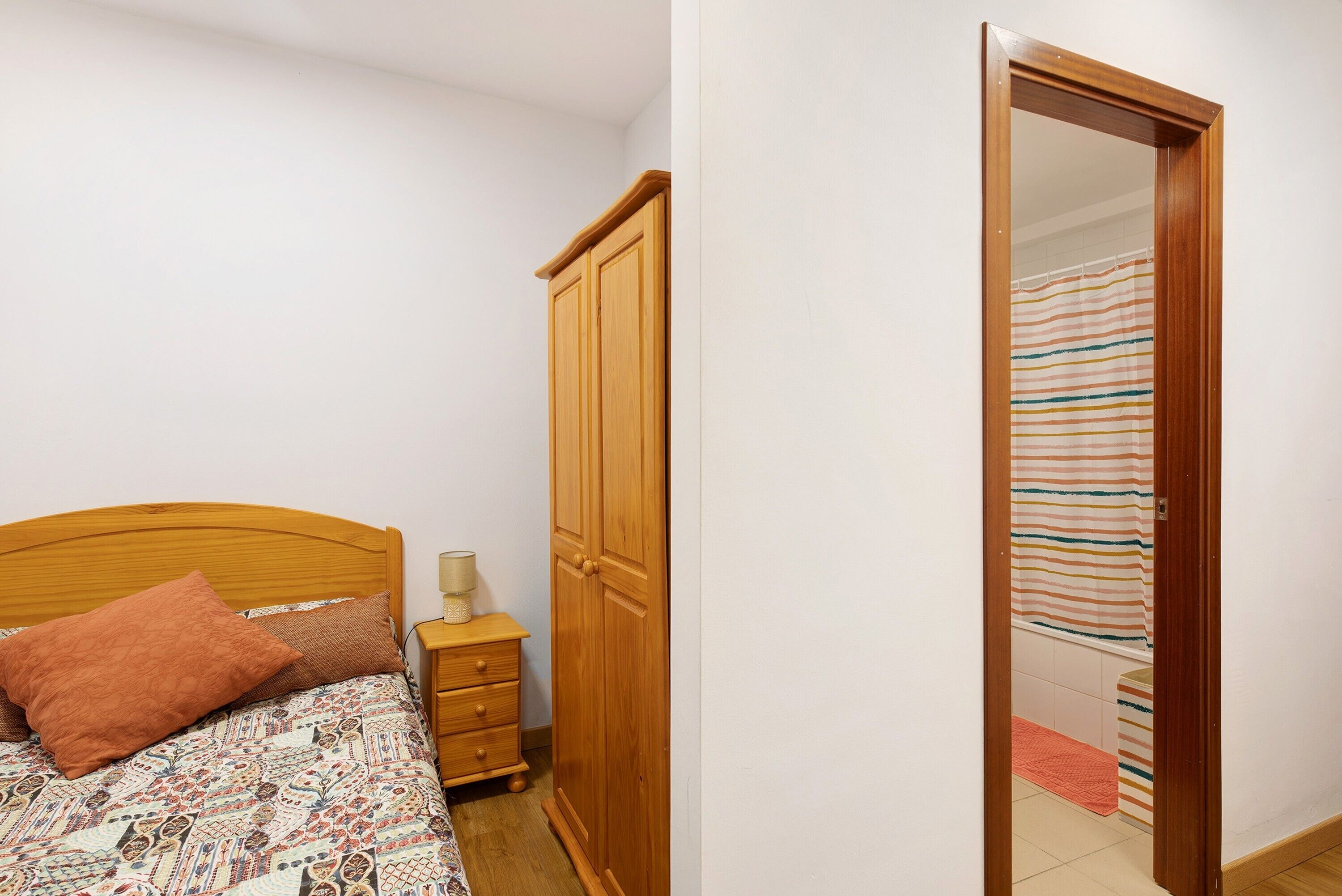 A bedroom with a wooden bed, a nightstand, a wardrobe, and a bathroom visible through an open door.