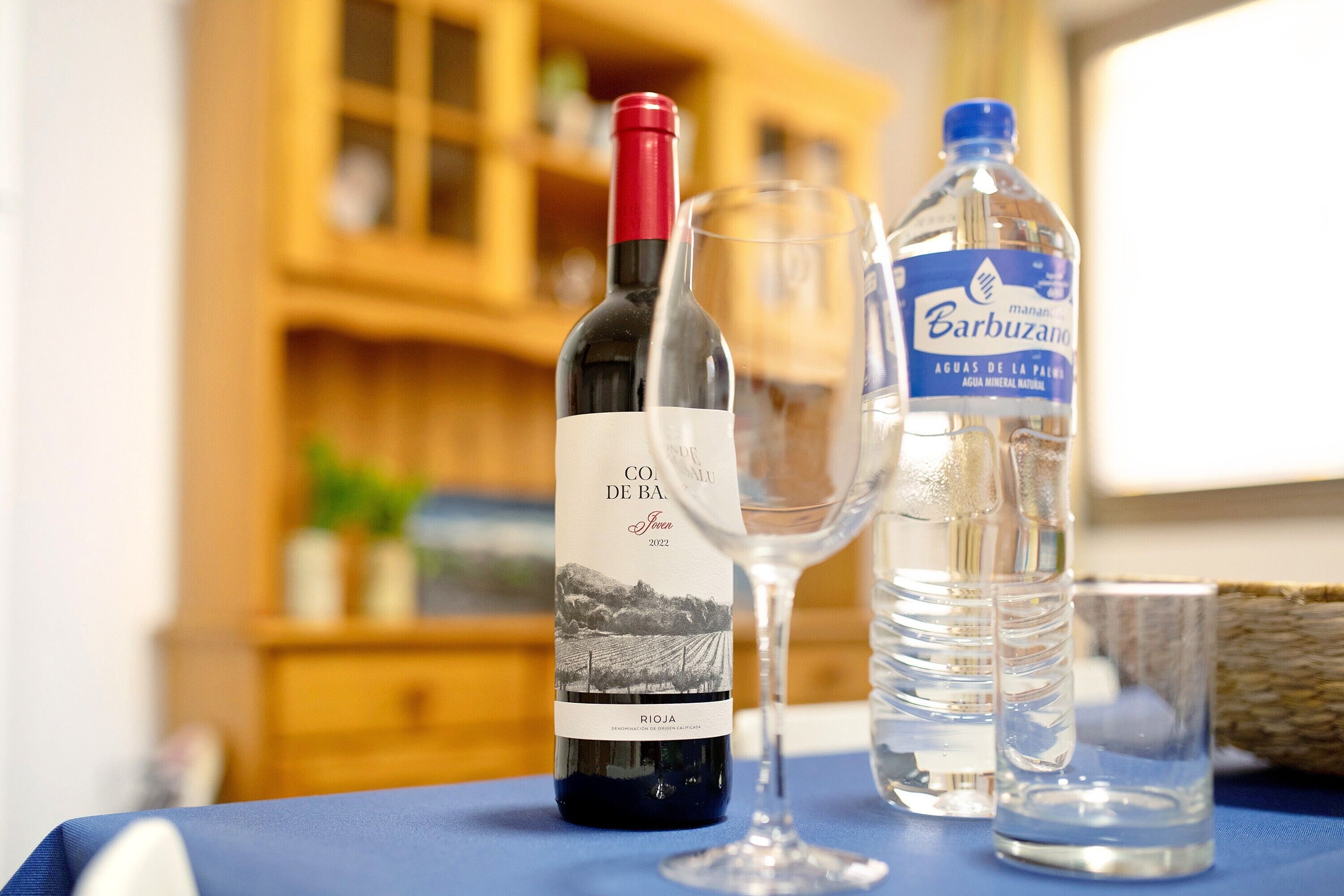 A bottle of wine, a glass, and a water bottle on a table.