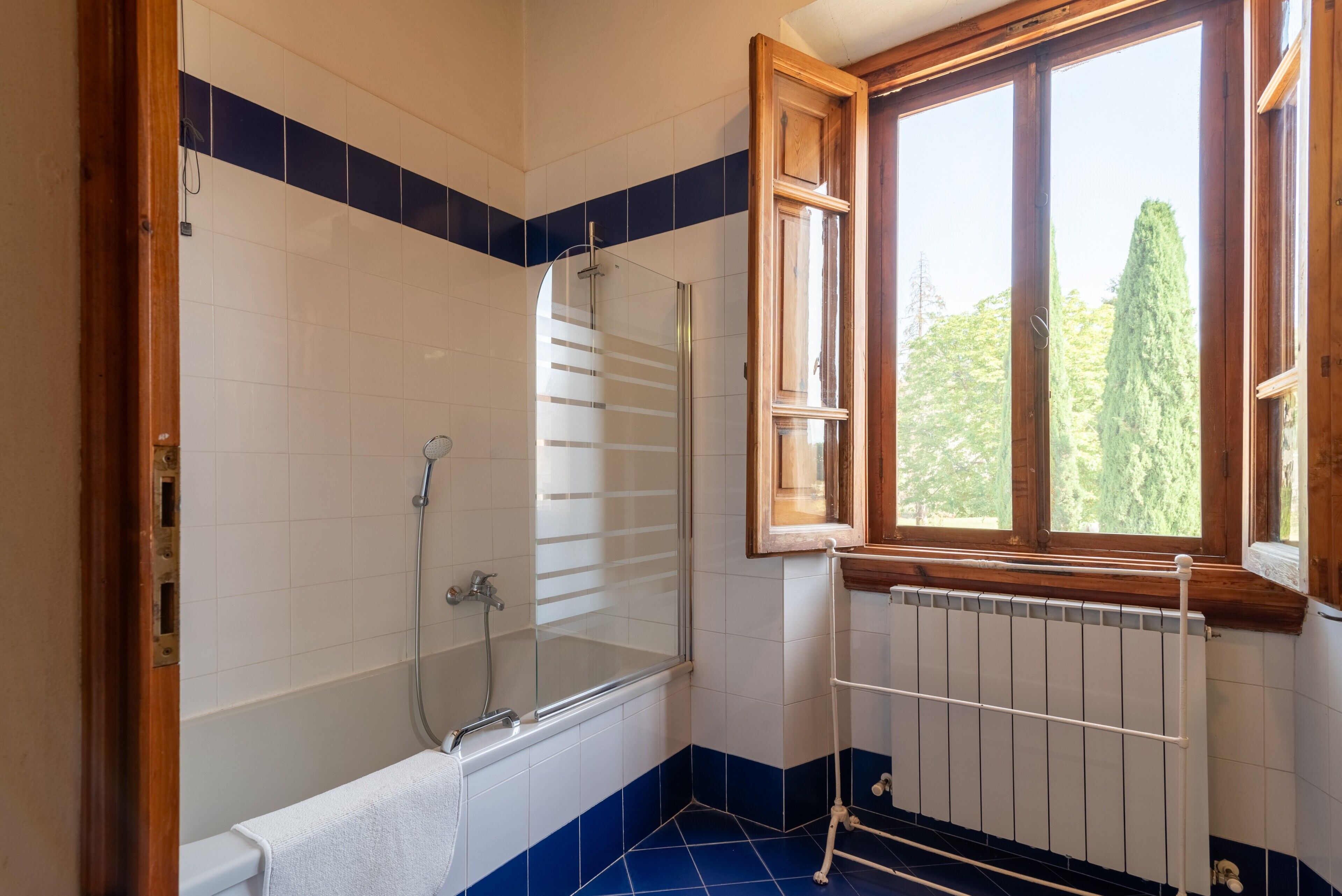 Un bagno con vasca, doccia e finestra vista alberi.