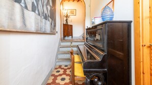 A hallway with a staircase, a wooden bench, a black piano, and a painting on the wall. - Farmhouse "Fattoria" with Shared Pool, Private Garden & Wi-Fi (Laterina)