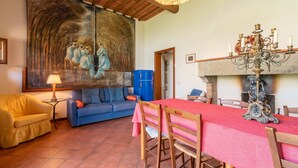 A dining area with a table set for four, a blue sofa, a yellow armchair, and a large painting on the wall. - Farmhouse 'Mulino ' with Shared Pool, Terrace & Wi-Fi (Laterina)