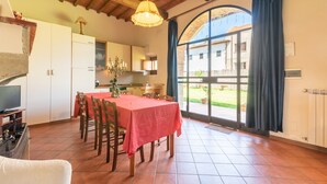 A dining area with a table set for four, a kitchen in the background, and a large window with curtains. - Farmhouse 'Mulino ' with Shared Pool, Terrace & Wi-Fi (Laterina)