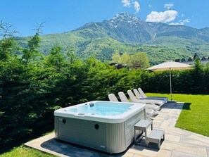 A hot tub with lounge chairs and a table, surrounded by a well-maintained lawn and a mountain view. - Casa Enea with private garden and mini pool (Colico)