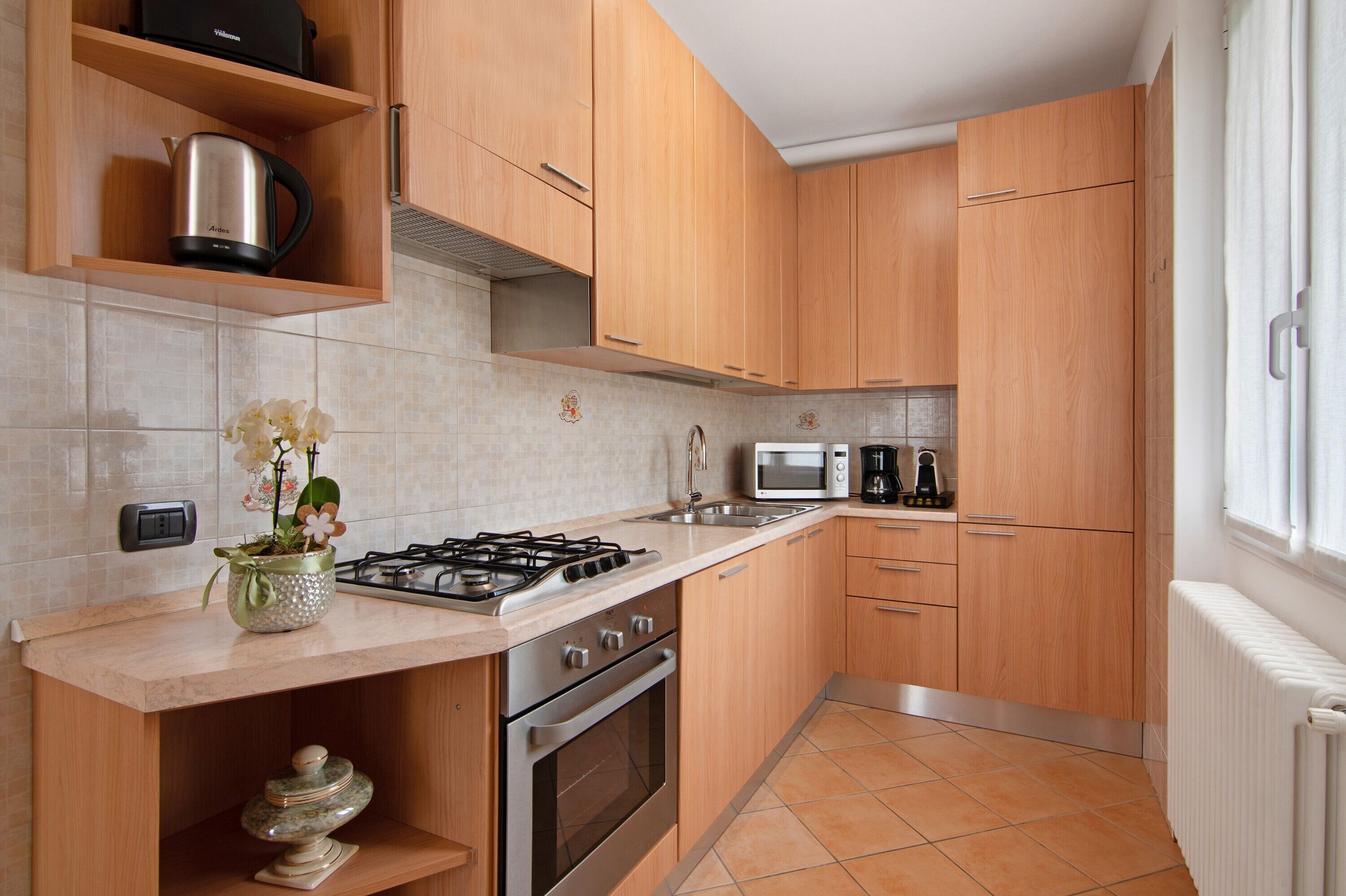 A modern kitchen with wooden cabinets, a gas stove, a microwave, and a kettle.