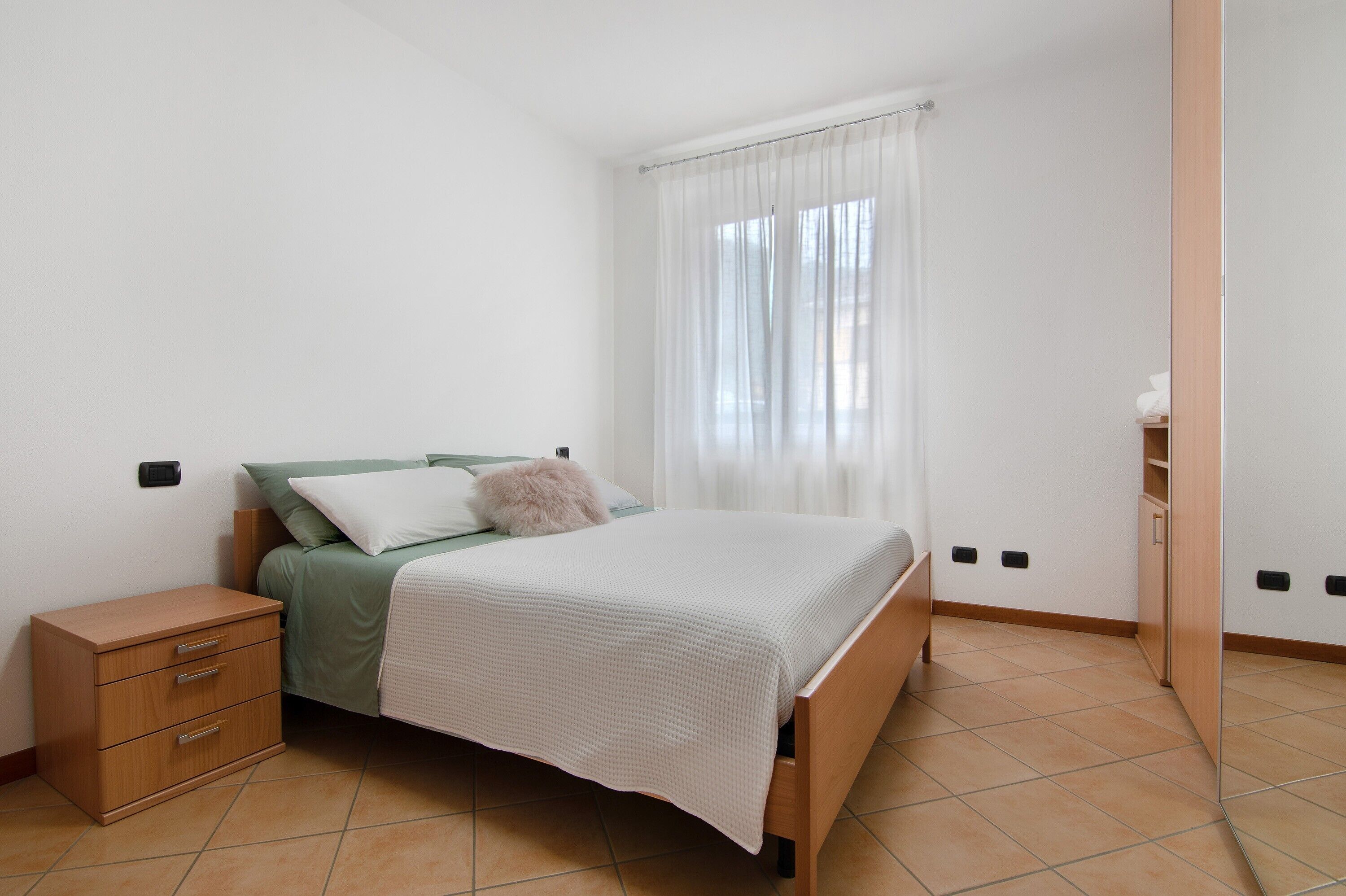 Une chambre à coucher comprenant un lit, une table de chevet, une armoire et une fenêtre avec des rideaux.