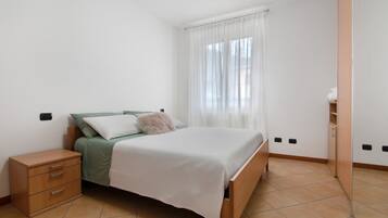 Une chambre à coucher comprenant un lit, une table de chevet, une armoire et une fenêtre avec des rideaux.
