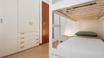 A bedroom with a bunk bed, a wooden door, a white wardrobe, and a bedside table.