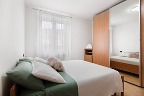 A bedroom with a bed, a wardrobe, a mirror, and a window with curtains.