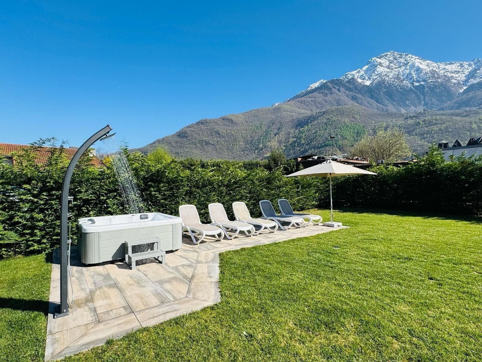 Ein Whirlpool, Liegestühle und ein Sonnenschirm im Garten mit Blick auf die Berge.