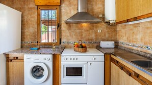 A kitchen with a washing machine, oven, and a window with a view. - Holiday Home 'Ladera De Los Molinos' with Mountain View, Pool, Garden & Wi-Fi (Padul)