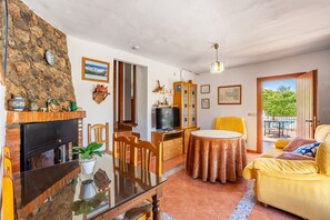 Un salon avec une cheminée, une table à manger, un canapé et une vue sur la verdure grâce à une porte coulissante.