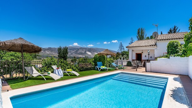 A swimming pool with lounge chairs, a thatched umbrella, and a view of mountains. - Holiday Home 'Ladera De Los Molinos' with Mountain View, Pool, Garden & Wi-Fi (Padul)