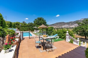 A patio with a table, chairs, a pool, and a view of the mountains.