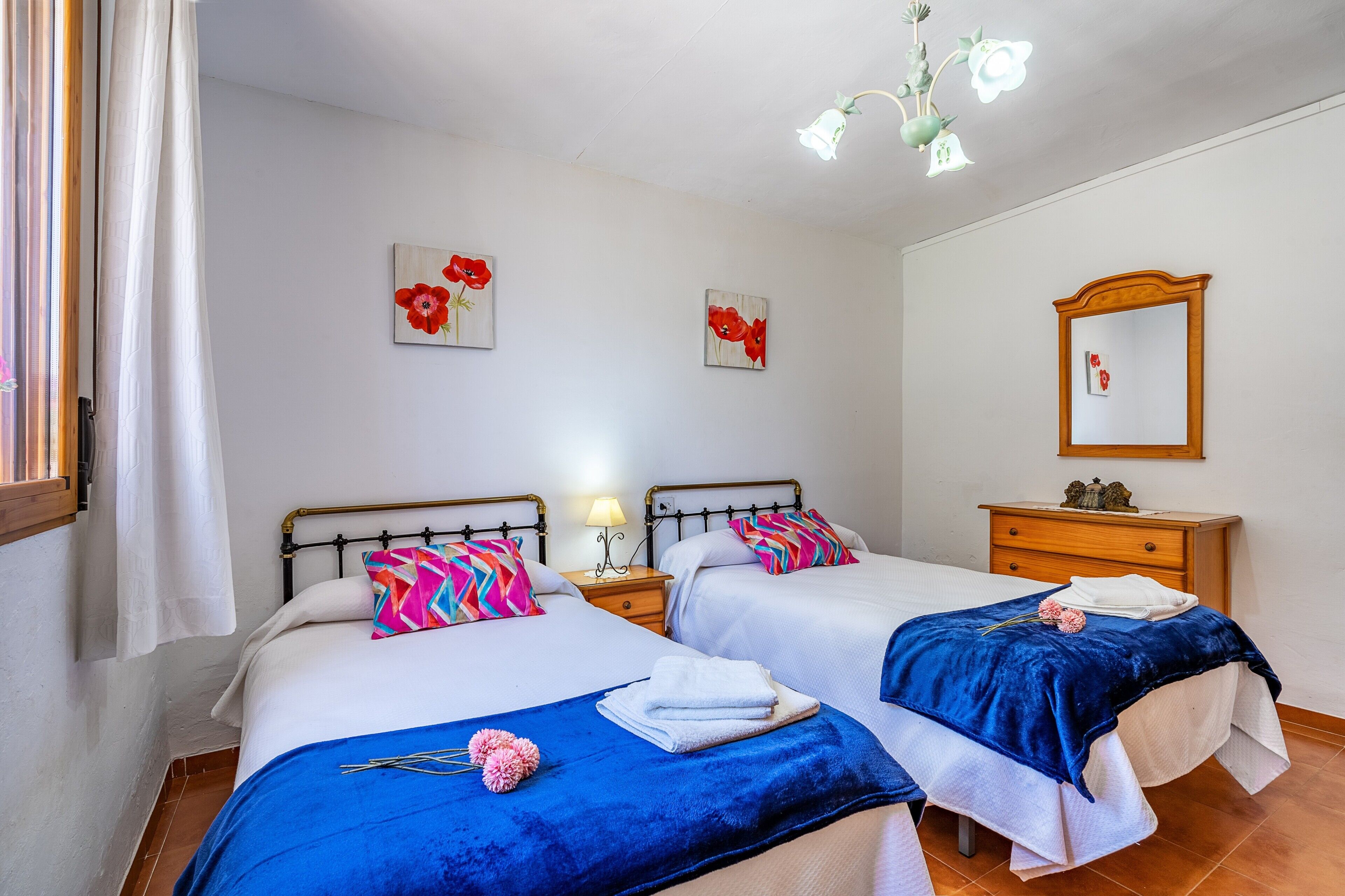 A hotel room with two beds, a nightstand with a lamp, a dresser, and a mirror on the wall.