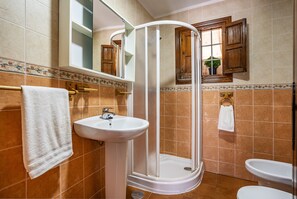 A bathroom with a shower, sink, and toilet, featuring tiled walls and wooden cabinets.