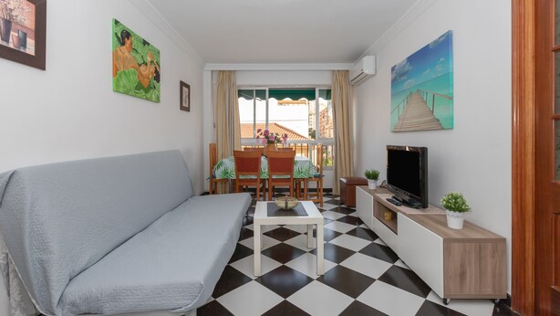 A furnished room with a sofa, a dining table with chairs, a TV, and artwork on the walls.