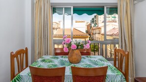 A dining area with a table, chairs, a vase with flowers, and a view of buildings through a window.