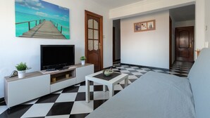 A room with a TV, a checkered floor, a bed, a wooden door, and a painting of a pier.