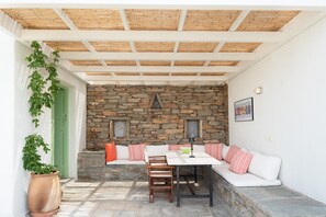Eine überdachte Terrasse mit einer Steinwand, Holzbalkendecke und einer Sitzecke mit Kissen.