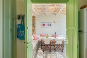 Puerta abierta que da a una habitación con pared de piedra, una mesa con sillas y una puerta verde.