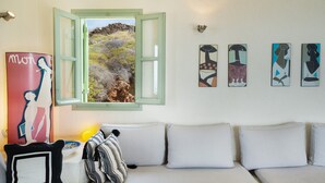 Een kamer met een witte bank, een raam met groene luiken en vier abstracte schilderijen aan de muur.