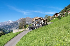 Un chalet à plusieurs étages doté d’un balcon, situé sur une colline avec une vue sur les montagnes.