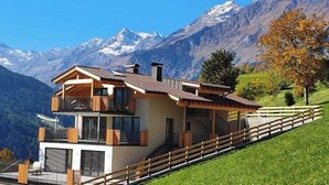 A modern two-story house with a balcony, set against a mountainous backdrop. - Apartment 'Sunnseitn Lodge Alps' with Mountain View, Private Terrace and Wi-Fi (Moos in Passeier)