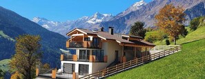 Une maison moderne à deux étages, dotée d’un balcon, qui se dresse sur un fond de paysage montagneux.