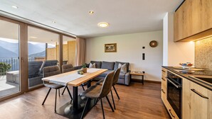 A modern kitchen with wooden cabinets, a dining area with a table and chairs, and a view of mountains through large windows. - Apartment 'Sunnseitn Lodge Alps' with Mountain View, Private Terrace and Wi-Fi (Moos in Passeier)