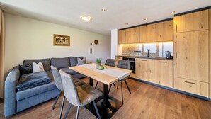 A modern living space with a dining table, grey sofa, and wooden kitchen cabinets. - Apartment 'Sunnseitn Lodge Alps' with Mountain View, Private Terrace and Wi-Fi (Moos in Passeier)