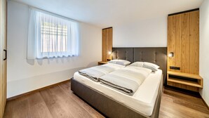 A modern bedroom with a bed, wooden headboard, built-in shelving, and a window with sheer curtains. - Apartment 'Sunnseitn Lodge Alps' with Mountain View, Private Terrace and Wi-Fi (Moos in Passeier)