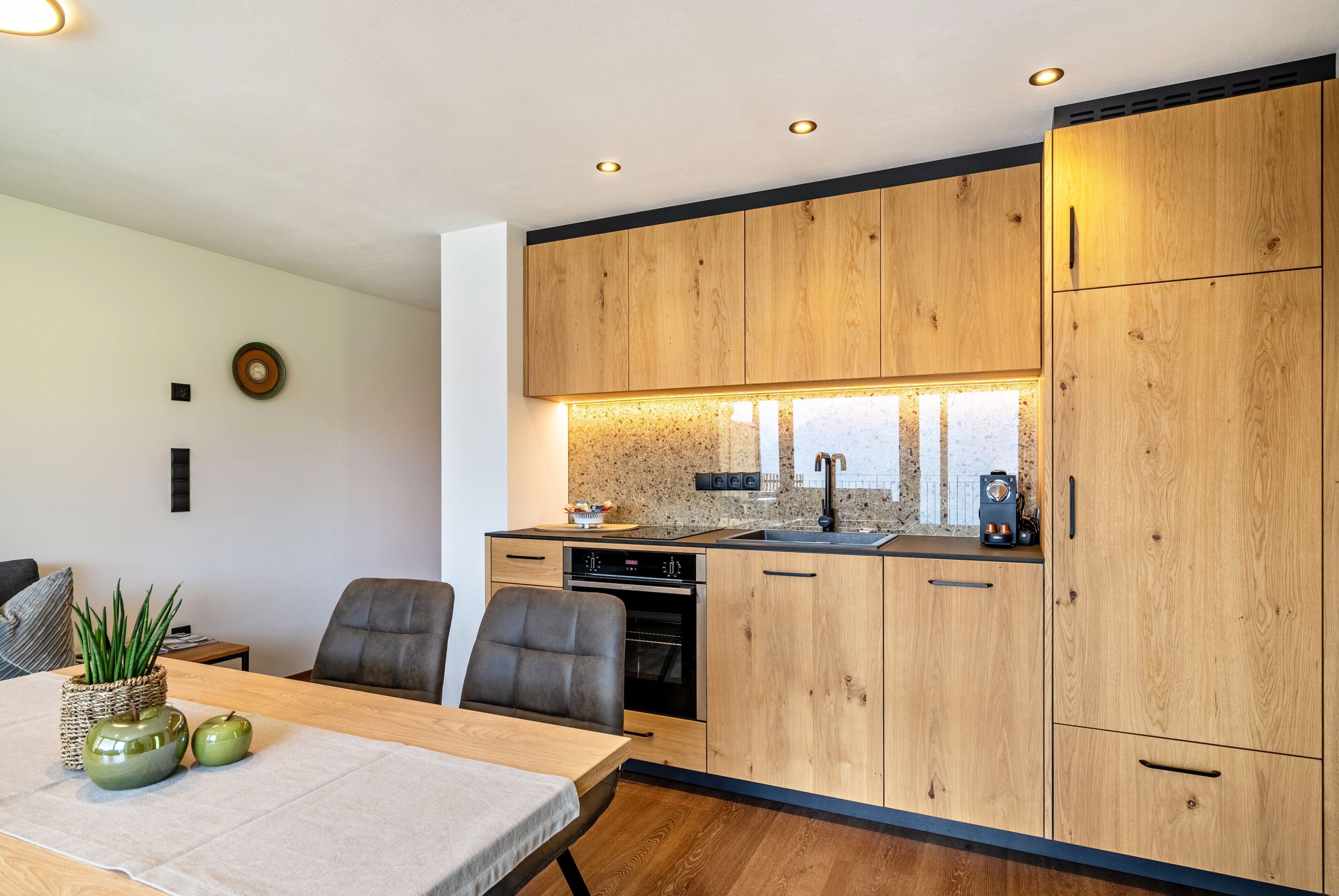 A modern kitchen with wooden cabinets, a dining table with chairs, and a built-in oven.